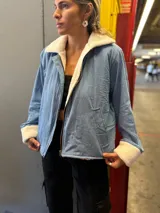 Campera de jean celeste con interior y cuello de corderito color crema, cierre frontal con cremallera y bolsillos laterales.