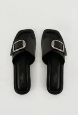 Sandalias planas de símil cuero negro con puntera cuadrada, pala ancha y hebilla metálica plateada de gran tamaño.