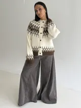 Cardigan de punto con diseño jacquard de inspiración nórdica, en tonos blanco, gris y marrón. Presenta cuello redondo, cierre frontal con botones y mangas largas con puños acanalados.