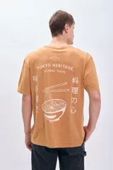 Remera color ocre de corte amplio con estampa en la espalda que incluye un plato de ramen, palillos y texto en inglés y japonés.