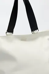 Bolso negro tipo shopper de símil cuero con terminación suave. Tiene asas anchas de cinta y un bolsillo frontal con solapa.
