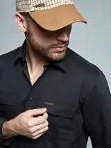 Camisa de manga larga color negro, con cuello clásico y dos bolsillos frontales con solapa. Presenta un pequeño aplique metálico decorativo en uno de los bolsillos.