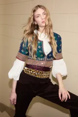 Camisa de seda con diseño tipo chaqueta corta, de color azul petróleo con bordados decorativos en tonos dorados y rojos. Presenta mangas largas abullonadas de color crema y cierre frontal.