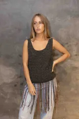 Musculosa tejida en punto calado color negro con destellos brillantes, presenta un diseño de flecos largos en el ruedo que combinan tonos rojizos, dorados y oscuros.