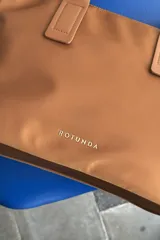Cartera tipo shopper color negro, de diseño estructurado con doble asa de mano y cierre superior. Presenta sutil grabado de la marca en la parte inferior frontal.