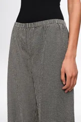 Pantalón de corte recto y tiro medio, con estampa de cuadros en blanco y negro. Posee cintura elástica y detalles de lazos ajustables en los tobillos.