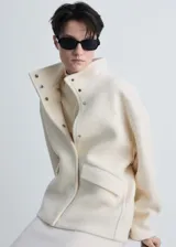 Chaqueta de corte recto confeccionada en mezcla de lana y viscosa, color crema. Presenta cuello alto, cierre frontal con botones ocultos, manga larga y dos bolsillos con solapa en la parte delantera.