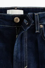 Jean de tiro alto con corte acampanado desde la rodilla, confeccionado en denim azul oscuro con costuras en contraste y diseño de cinco bolsillos.