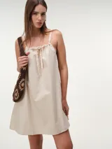 Vestido corto de popelina de algodón color arena, con diseño fluido, breteles finos y detalle de lazo ajustable en el escote.