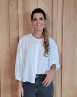 Camisa blanca de manga tres cuartos con puños elásticos, cuello redondo y cierre frontal con botones nacarados. Presenta un delicado estampado floral en relieve sobre toda la prenda.