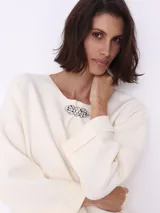 Sweater color crema de tejido de punto, con cuello redondo y prendedor de strass.