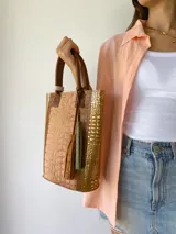 Bolso matero de cuero color beige con textura tipo piel de cocodrilo, detalles en cuero color marrón y borlas decorativas.