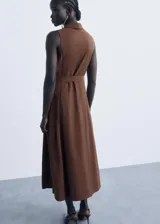 Vestido midi de color marrón, con diseño evasé, cuello camisero y cierre frontal con botones. Presenta un cinturón ajustable a la cintura y un diseño sin mangas con tirantes anchos.