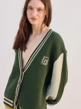 Cardigan oversize de punto color verde oscuro con detalles en tonos tierra, escote en V y cierre frontal de botones. Cuenta con paneles en contraste en las mangas y un parche bordado en el pecho.