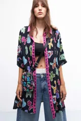 Porta celular negro con estampado de sirenas, langostas y peces en tonos rosa, rojo, verde y azul. Tiene correa larga regulable de tela negra y cierre con solapa y botón imantado.