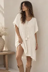Poncho corto de tejido de punto color beige, con escote en V acordonado con cordones terminados en borlas y mangas cortas holgadas.