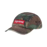 Gorro tipo camp cap de la marca Supreme con estampado de camuflaje y parche rectangular rojo con el logo de la marca bordado en blanco en la parte frontal.