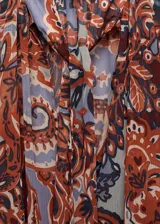 Vestido corto con estampado paisley en tonos marrón, naranja, celeste y lila. Tiene cuello redondo con lazo, mangas largas acampanadas, forro interior y cinturón desmontable.
