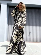 Vestido largo tipo túnica con estampado de hojas en contraste blanco y negro. Presenta cuello camisero con botones, mangas largas amplias y falda con volados escalonados.