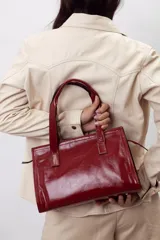 Cartera mini tote de cuero vacuno color bordó, con acabado charol, doble asa de mano y estructura rígida.