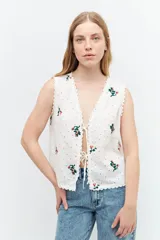 Chaleco blanco de broderie con bordados florales, escote en V y cierre con lazos.