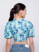 Top estampado con flores rosas, hojas verdes y líneas negras, de manga corta abullonada con nudo en el escote.