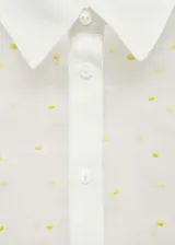 Camisa de manga corta con diseño recto y cuello camisero. Confeccionada en tejido semitransparente con bordado de flores pequeñas y cierre frontal con botones.