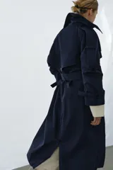 Trench oversize de Zara Woman Collection, color azul marino, confeccionado en hilatura con mezcla de algodón. Presenta cuello solapa, manga larga ajustable con trabillas, bolsillos delanteros y cinturón del mismo tejido con lazadas. Destacan los pespuntes marcados a tono y el cierre frontal cruzado con botones.