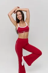 Conjunto deportivo compuesto por un top y un pantalón largo de corte acampanado, ambos en color rojo con detalles de líneas blancas. El top presenta breteles finos y el logo 'bk.' estampado en el frente. El pantalón cuenta con una línea lateral blanca y aberturas en el ruedo.