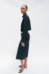 Bermuda larga de tiro alto en tejido de denim azul oscuro, con diseño de pernera recta y ancha, y detalles de botones metálicos dorados en la parte delantera.