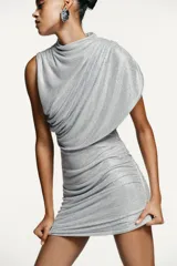 Vestido corto de tejido mesh plateado con aplicación de strass. Presenta cuello redondo, diseño sin mangas con drapeado en los hombros y una superposición efecto capa. Incluye frunces en los laterales y cierre oculto en el cuello.