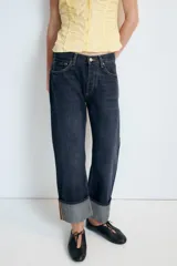 Jeans rectos de tiro medio en denim negro con efecto lavado. Presenta diseño de cinco bolsillos, trabillas para cinto y bajo con vuelta marcada. Cierre frontal con botones metálicos ocultos.
