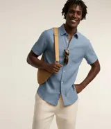 Camisa de manga corta confeccionada en mezcla de lino y algodón, con cuello inglés, cierre frontal de botones y bolsillo en el pecho. Presenta un corte comfort holgado y diseño liso.