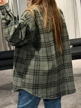 Camisa tipo sobrecamisa de corte oversize, confeccionada en tela a cuadros en tonos marrones y negros. Presenta cierre frontal con botones metálicos a presión, bolsillos frontales con solapa y mangas largas con puños abotonados.