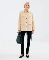 Chaqueta de corte recto color beige, con cuello camisero, cierre frontal de botones oscuros y cuatro bolsillos con solapa en el frente.