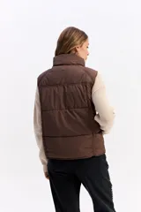 Chaleco puffer negro con cuello alto, cierre frontal y broches a presión. Diseño acolchado liviano con bolsillos laterales.