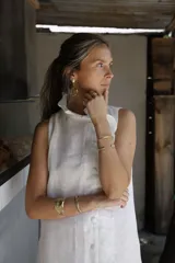 Vestido corto de lino sin mangas, con cuello alto adornado con un volado. Presenta un acceso frontal cruzado con botones forrados en la misma tela y un largo por encima de la rodilla.