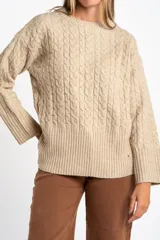 Sweater de punto con diseño de trenzas, color beige, de corte oversize, cuello redondo y mangas largas con puños anchos acanalados.