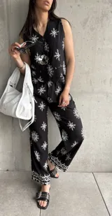 Chaleco negro con estampado de flores blancas, sin mangas, con cuello en V y cierre frontal con botones.