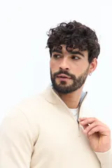 Sweater de tejido de punto color beige claro jaspeado, con cuello alto y cierre frontal parcial. Presenta puños y cuello acanalados.