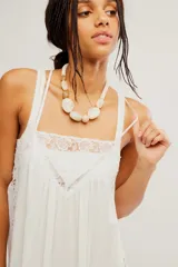Vestido largo slip blanco de tela liviana y semitransparente, con silueta trapecio, escote cuadrado, tiras regulables, detalles de encaje, volado en el ruedo y espalda descubierta con lazo de ajuste.
