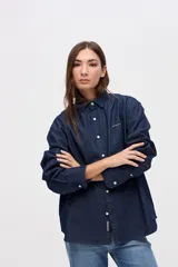 Camisa de algodón en color celeste claro, con cuello solapa, cierre frontal de botones y bordado pequeño en el pecho. Presenta un corte holgado y mangas largas.