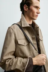 Sobrecamisa de corte boxy fit confeccionada en algodón con estructura canvas y efecto lavado. Presenta cuello solapa, cierre frontal con botones, mangas largas con puños abotonados y bolsillos de plastrón con solapa en el pecho. Incluye detalles bordados a tono en las mangas.
