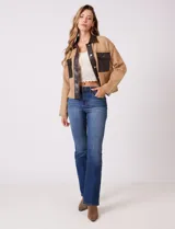 Chaqueta de corte boxy confeccionada en tejido de punto color crema, con detalles en cuero sintético negro en cuello, solapas, cartera central y bolsillos frontales. Presenta cierre frontal con botones metálicos plateados y costuras decorativas visibles.