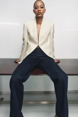 Blazer tipo frac de corte largo y diseño sin solapa. Presenta mangas largas con abertura, falsos bolsillos de vivo en el delantero y bajo asimétrico. Cuenta con cierre frontal mediante gancho metálico y forro interior a tono.