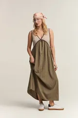 Vestido largo de silueta amplia y caída fluida, sin mangas, con escote en V y recorte bajo el busto. Combina un cuerpo superior beige con ribetes oscuros y una falda larga en color verde militar.