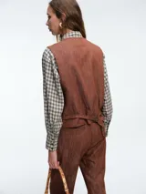 Chaleco estructurado de denim color terracota, con escote en V, cierre frontal con botones y bolsillos laterales tipo ojal.