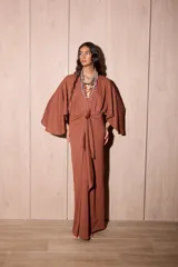 Vestido largo tipo kimono de color marrón, confeccionado en tela de punto texturada. Posee mangas amplias y abiertas, escote en V pronunciado y un lazo ajustable en la cintura para definir la silueta.