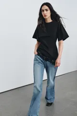 Camiseta de algodón compacto con cuello redondo y manga corta. Presenta un diseño de bajo asimétrico con aplicación de encaje a tono.