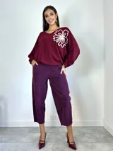 Sweater de punto oversized color verde, con escote en V y manga larga. Presenta un aplique bordado en forma de flor en el hombro izquierdo.